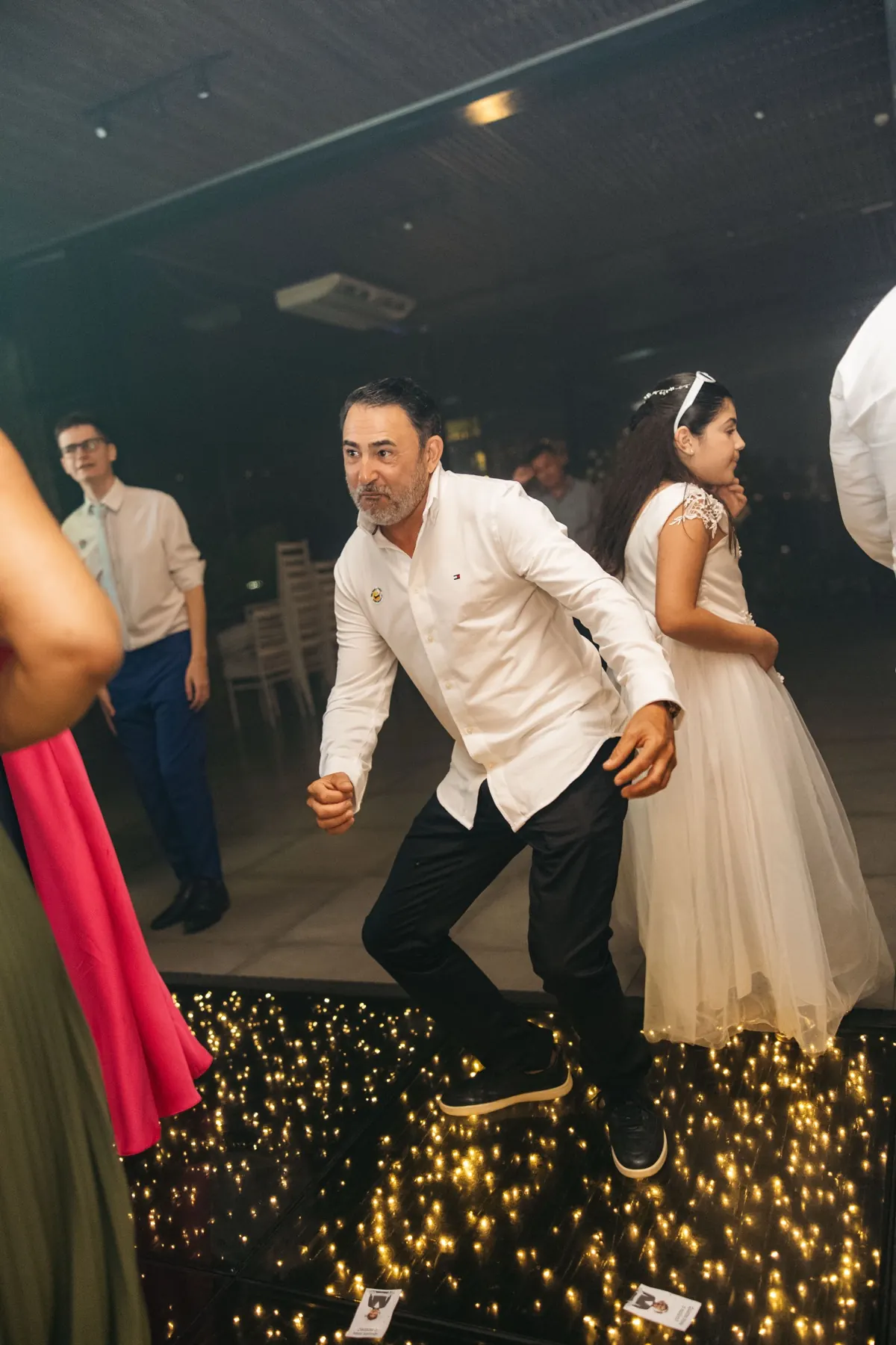 Convidado dança animado sobre a pista iluminada, com outros convidados ao redor.