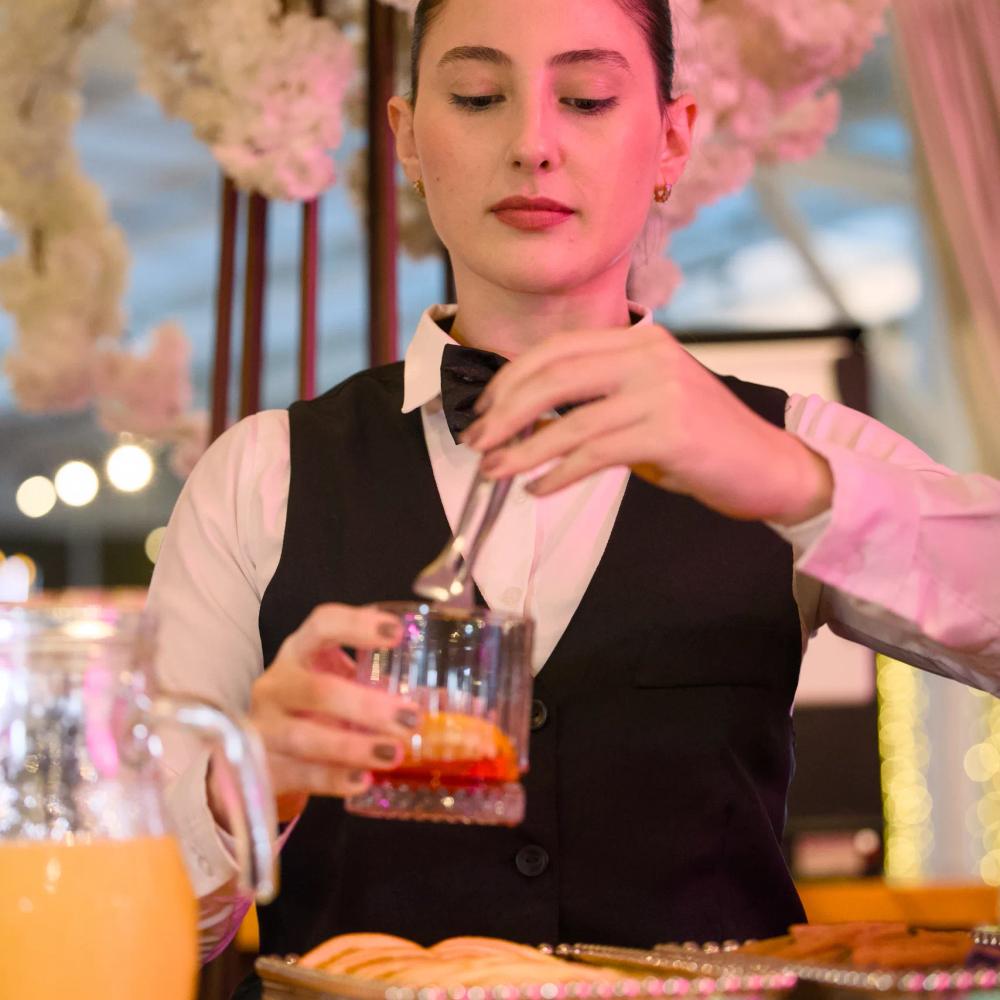Bartender da casa preparando um drink no bar, sob a decoração de flores