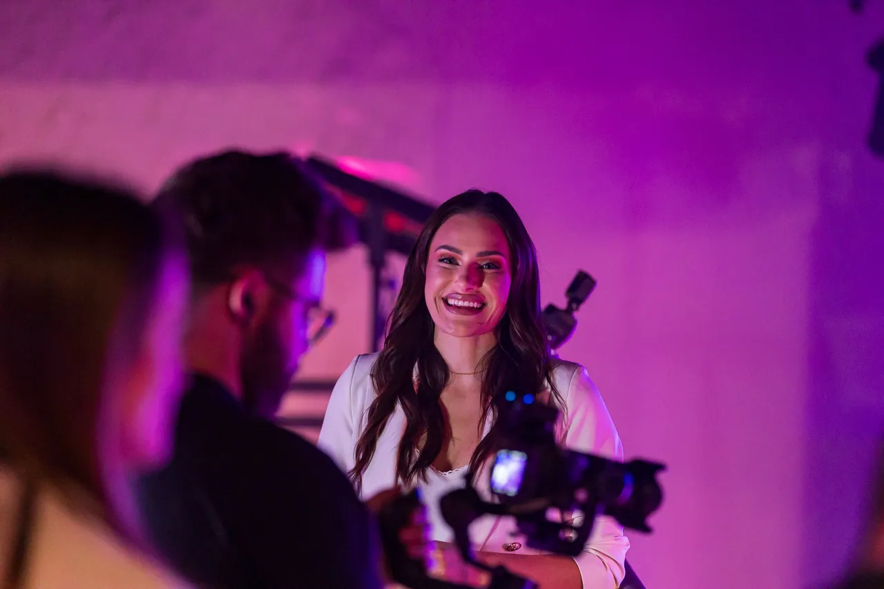 Participante sorrindo durante uma gravação em um evento corporativo no Indaiá, sob iluminação violeta.