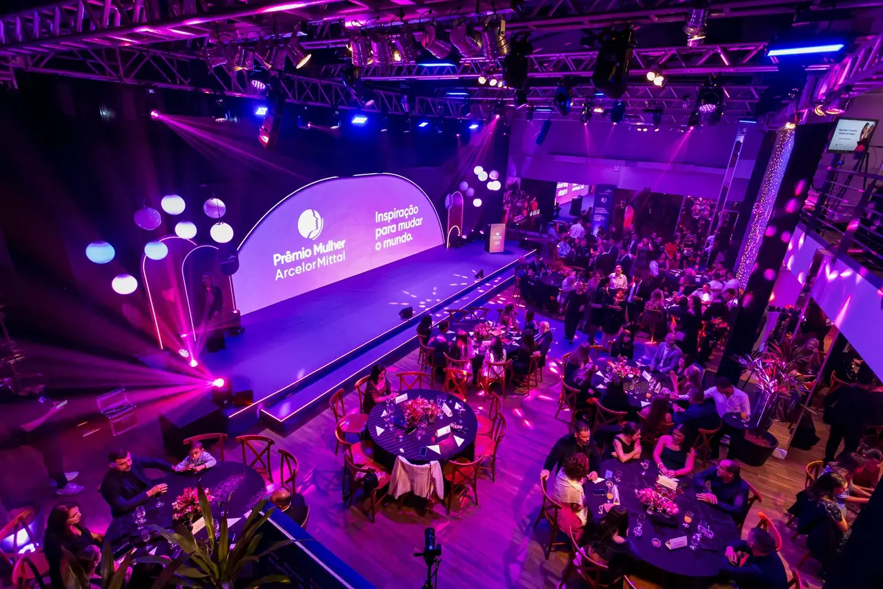 Evento corporativo com palco e mesas de convidados sob iluminação violeta.