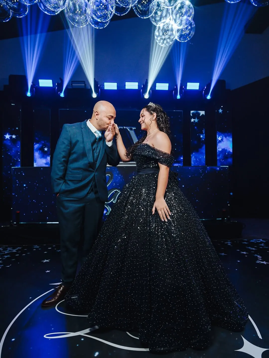 Debutante e acompanhante em um momento da celebração, sob luzes azuis e globos suspensos.