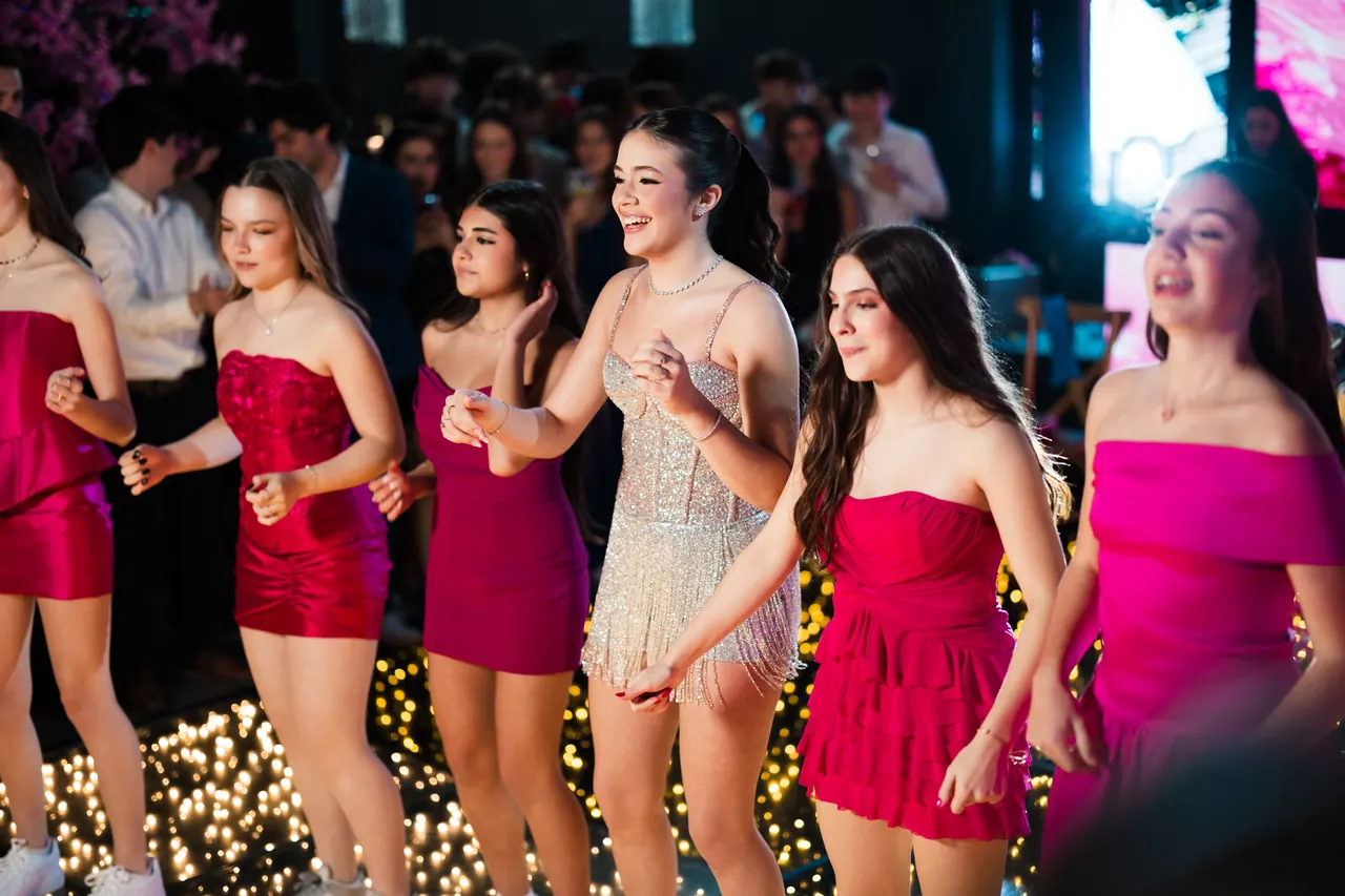 Debutante e amigas dançando juntas na pista iluminada da festa de 15 anos.