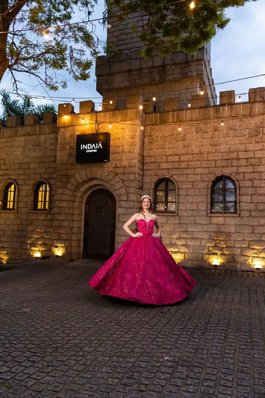 Debutante de vestido rosa diante do Castelo Blumenau do Indaiá, com cordões de luzes.