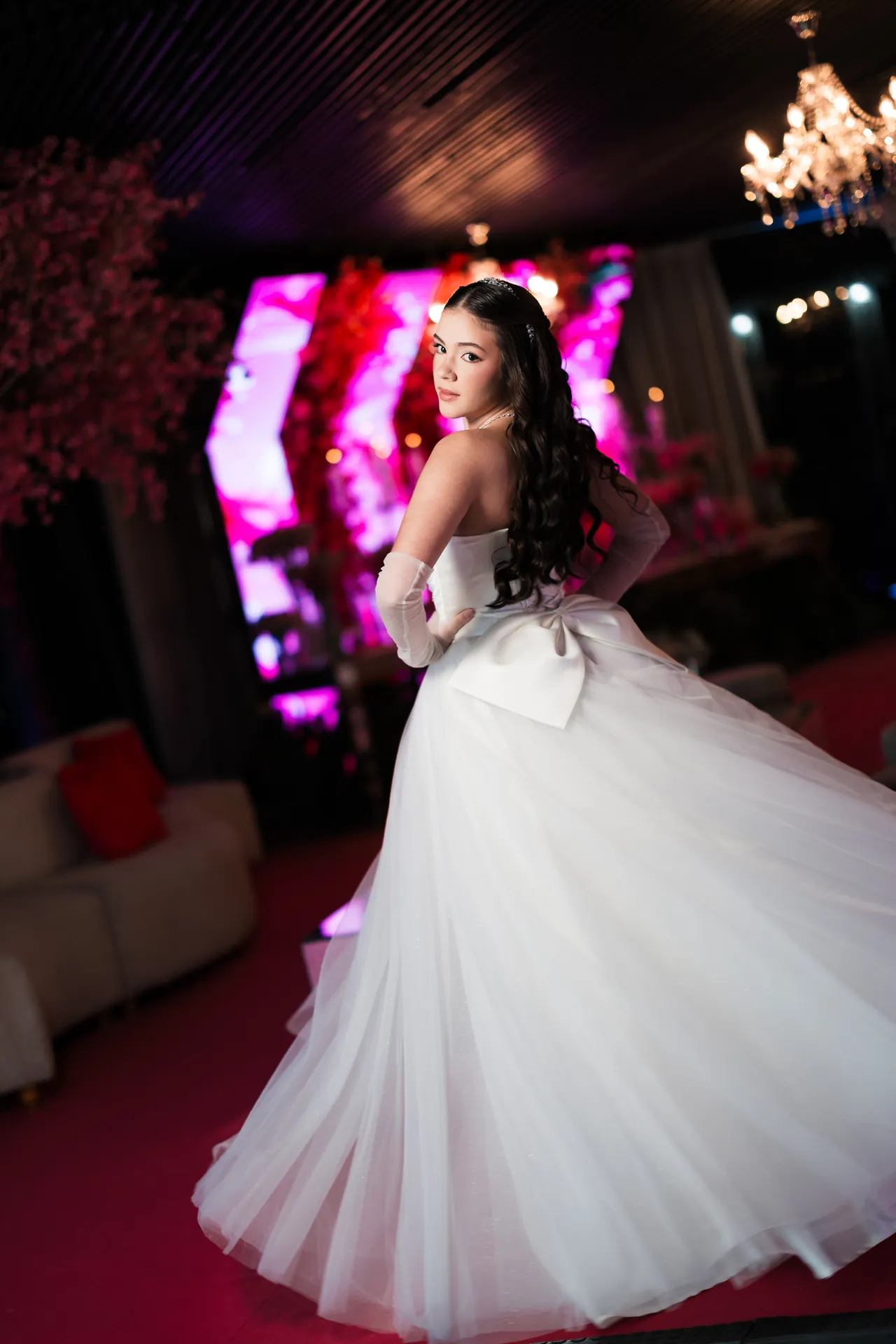 Debutante de vestido branco em uma celebração com flores e iluminação rosa, em Florianópolis.