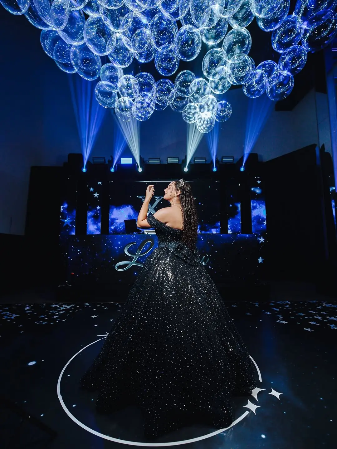 Debutante de vestido escuro na pista, sob globos transparentes e iluminação azul em Joinville.