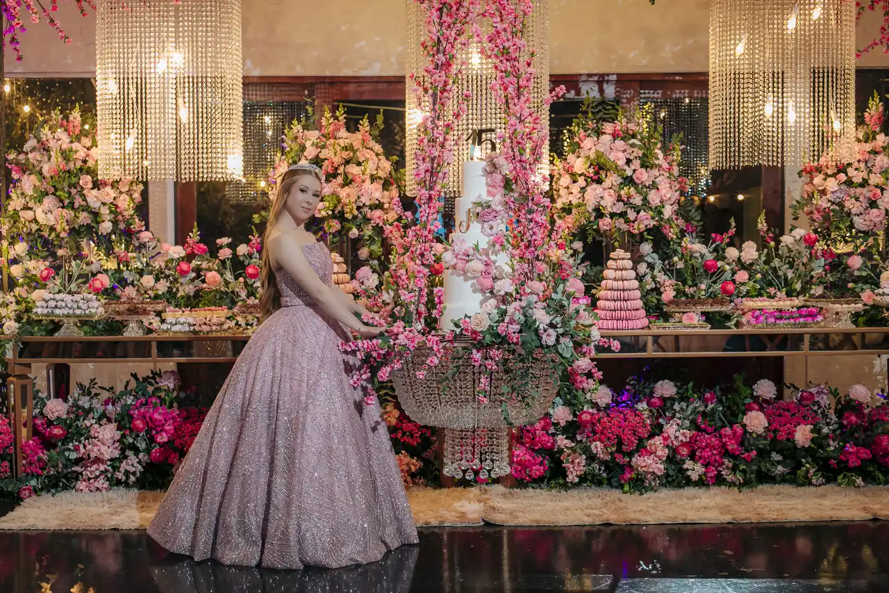 Debutante junto à mesa de bolo e flores no Salão de Eventos do Indaiá, em Itapema.